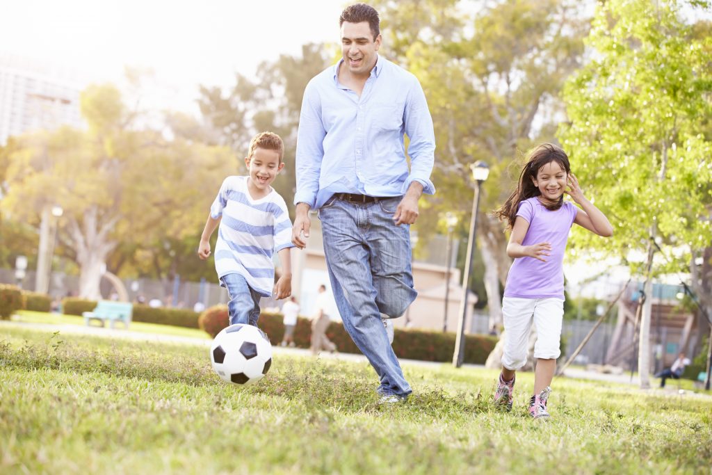Father With Children Playing Soccer In Park Together